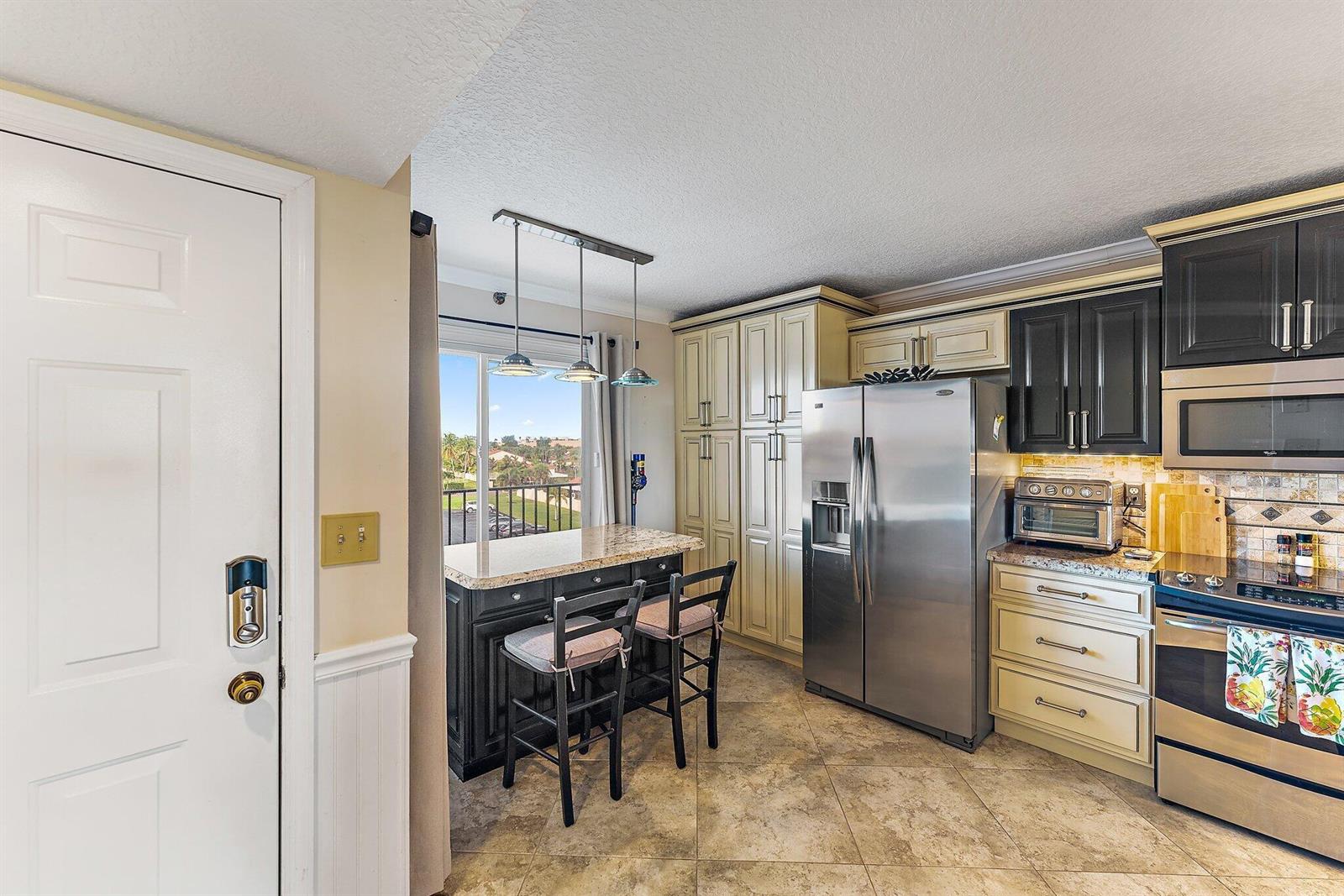 A kitchen features two-toned cabinetry, stainless steel appliances, a granite-topped island, and a balcony view — 275 Palm Avenue # C402, Jupiter FL 33477, JUPITER, FL