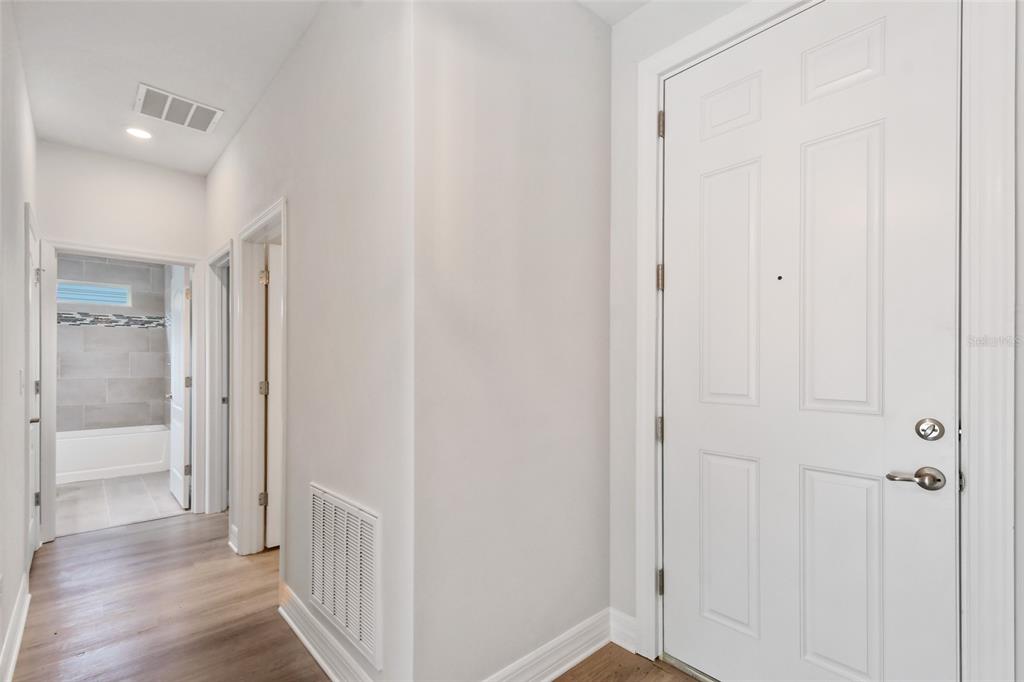 A white front door opens into a hallway with wood-look flooring and a bathroom beyond — 407 W HARVARD STREET, INVERNESS, FL