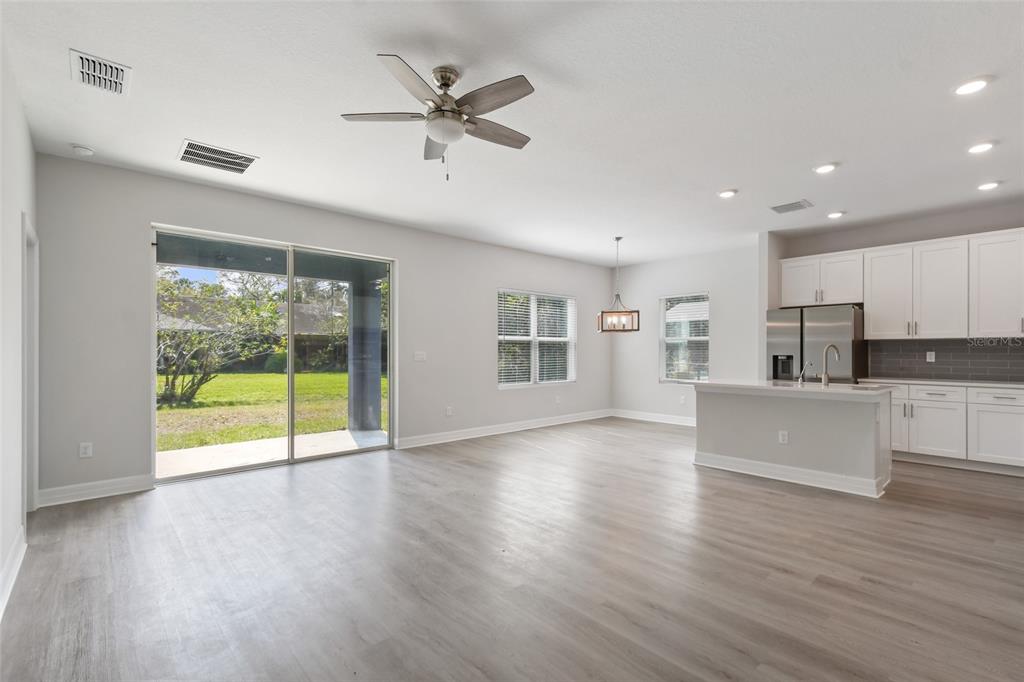 An open-concept living and dining area features light wood-look flooring, white cabinets, and sliding doors — 407 W HARVARD STREET, INVERNESS, FL