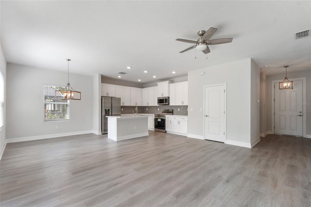An open-concept kitchen and dining area features white cabinetry, stainless steel appliances, and wood-look flooring — 407 W HARVARD STREET, INVERNESS, FL