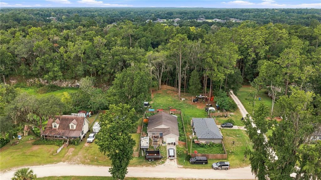 An aerial view shows three houses situated along a dirt road surrounded by dense trees — 2460 SE 69TH LANE, OCALA, FL