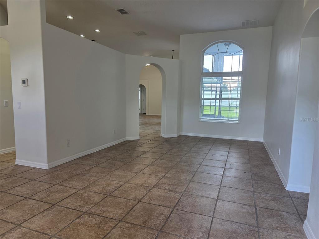 An empty room features beige tile flooring, white walls, an arched doorway, and a large window — 881 SENECA TRAIL, ST CLOUD, FL