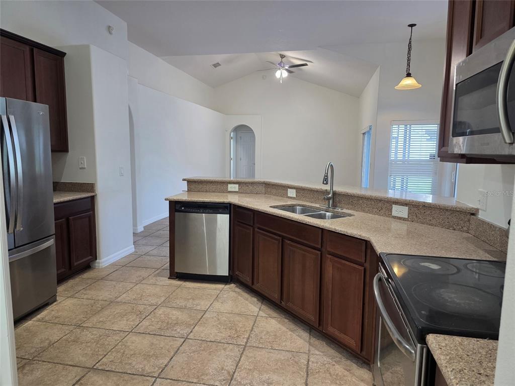 A kitchen features dark wood cabinets, granite countertops, stainless steel appliances, and tile flooring — 881 SENECA TRAIL, ST CLOUD, FL