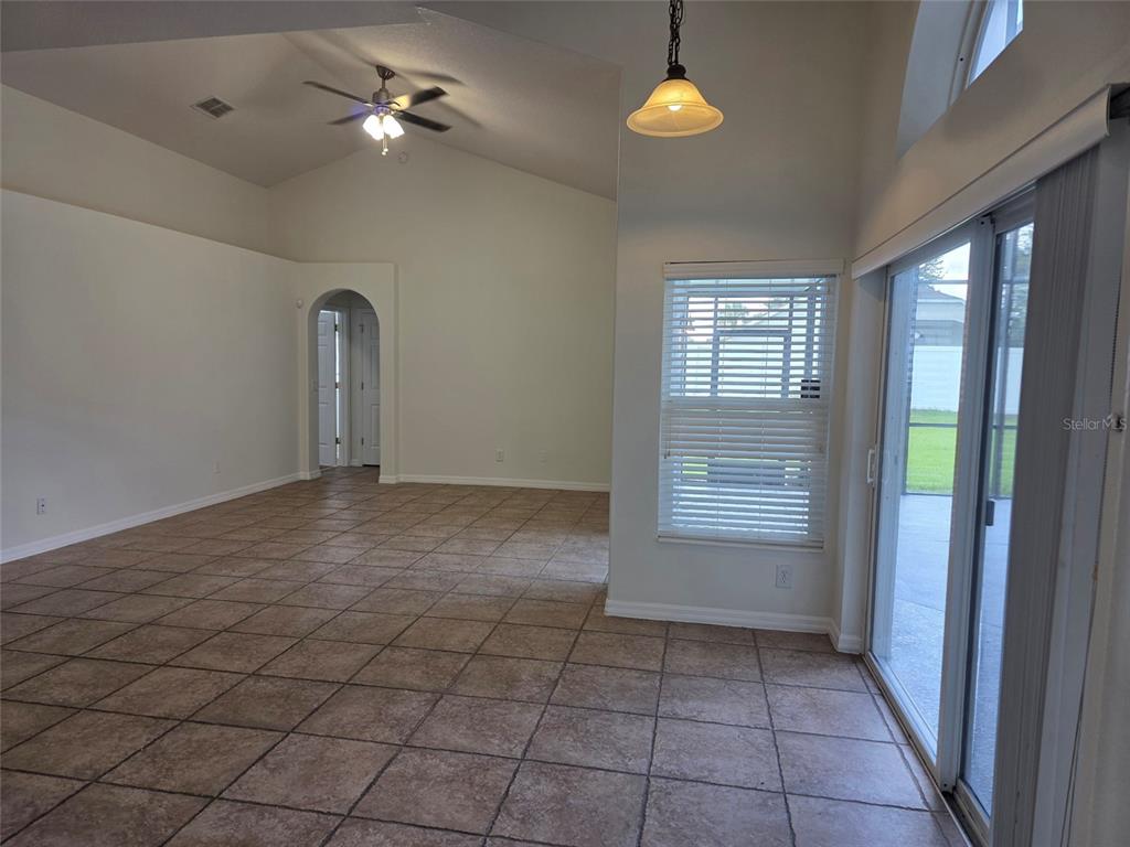An open-concept living area features vaulted ceilings, tile flooring, and a sliding glass door — 881 SENECA TRAIL, ST CLOUD, FL