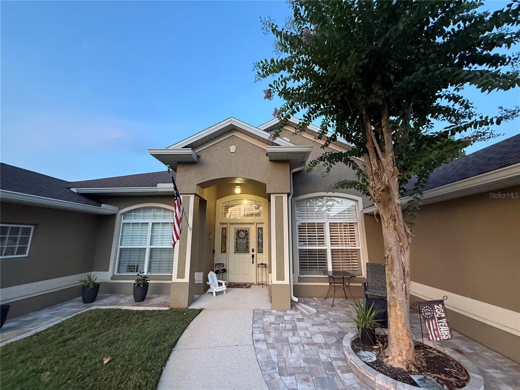 The exterior of a single-story house features a paved walkway, a tree, and an American flag — 12734 COLONNADE CIRCLE, CLERMONT, FL
