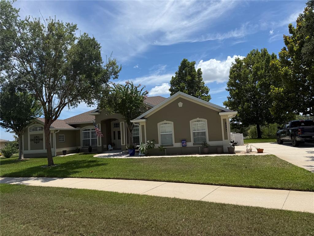 A single-story house with a tan exterior, a paved driveway, and a manicured front lawn — 12734 COLONNADE CIRCLE, CLERMONT, FL
