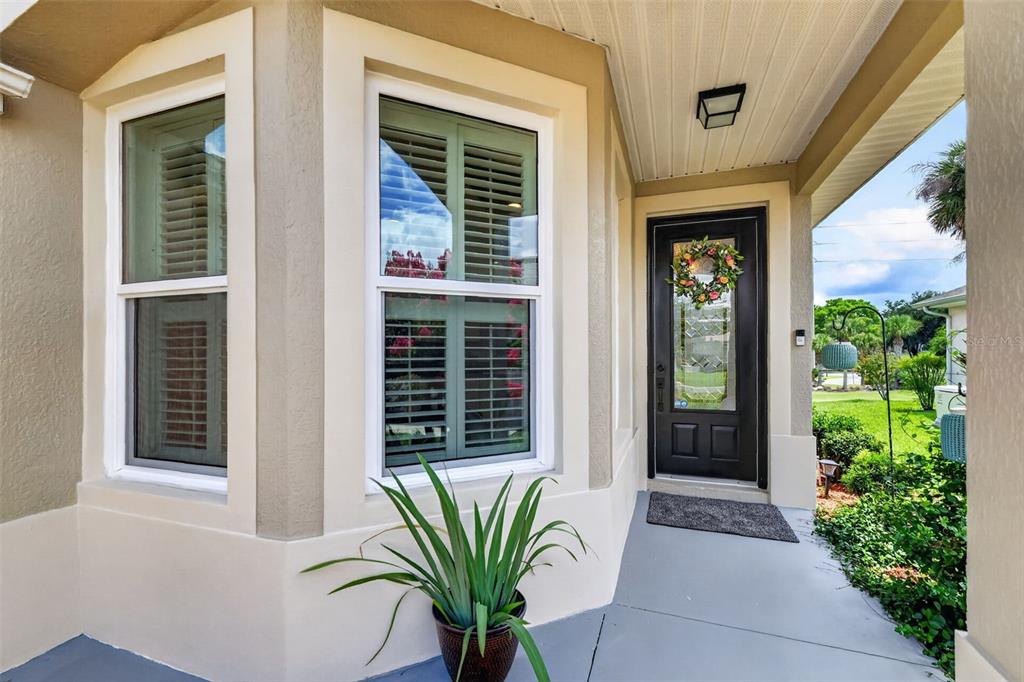 A covered front porch features a black door with a wreath and two bay windows — 5304 TREASURE VIEW WAY, LEESBURG, FL