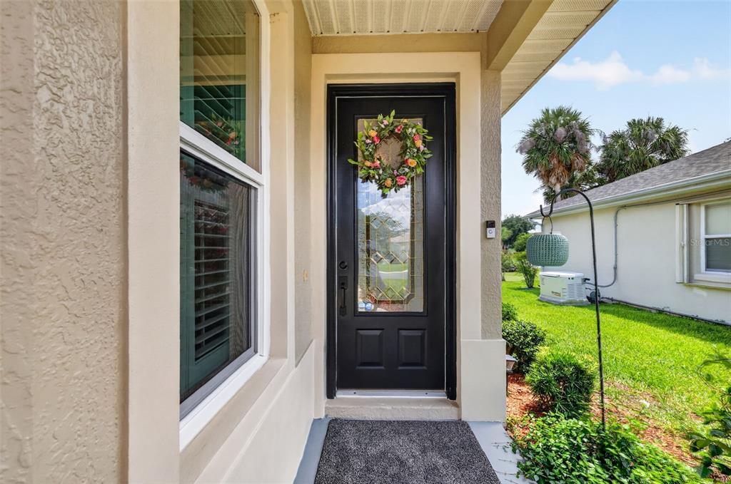 A black front door with a glass insert and floral wreath sits under a porch — 5304 TREASURE VIEW WAY, LEESBURG, FL