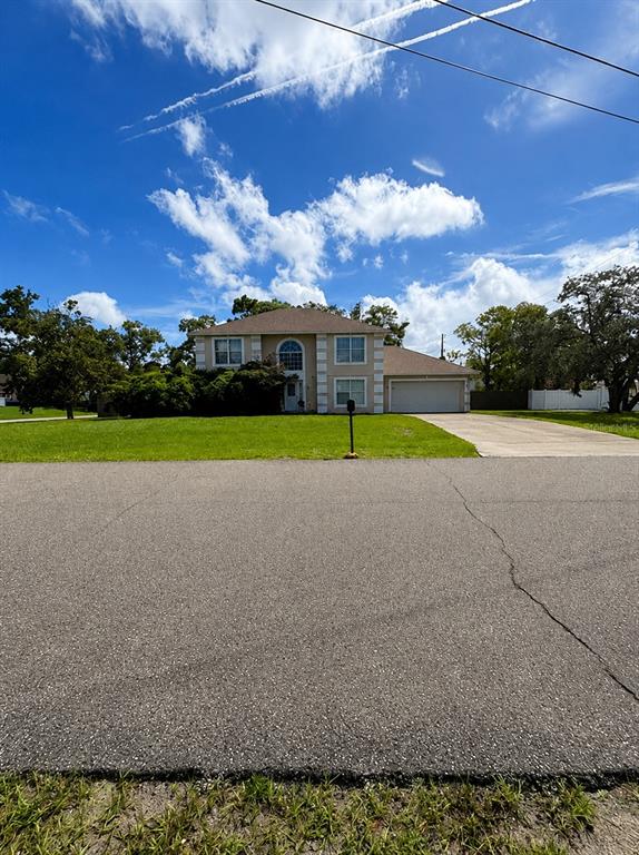 A two-story suburban house with a tan exterior, a front lawn, and a concrete driveway — 2254 MARBLE AVENUE, SPRING HILL, FL