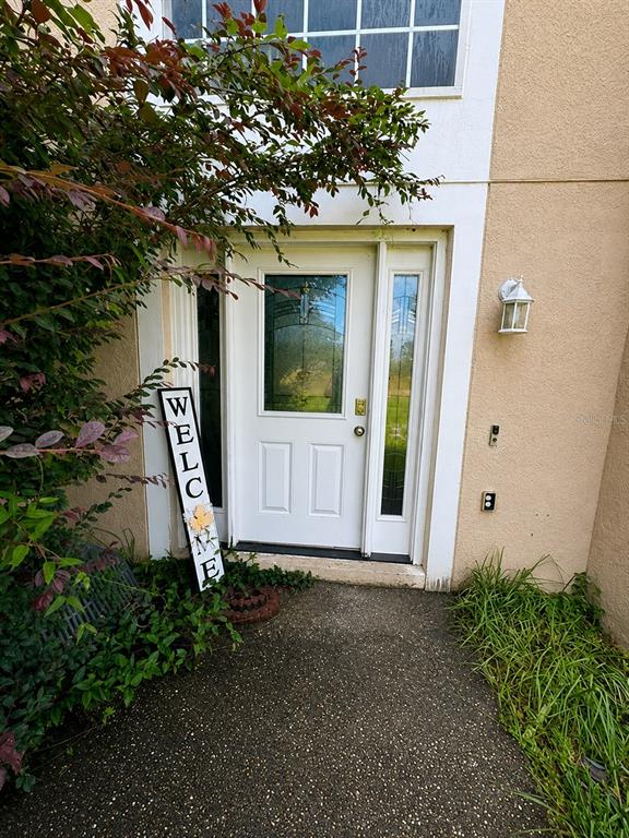 A white front door with glass panels is flanked by a welcome sign and landscaping — 2254 MARBLE AVENUE, SPRING HILL, FL