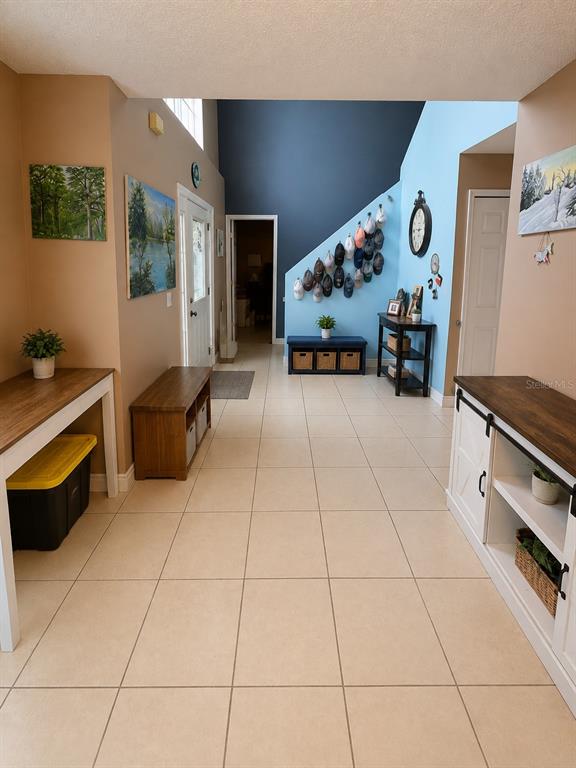 A tiled entryway features a high ceiling, a blue accent wall, and wooden furniture pieces — 2254 MARBLE AVENUE, SPRING HILL, FL