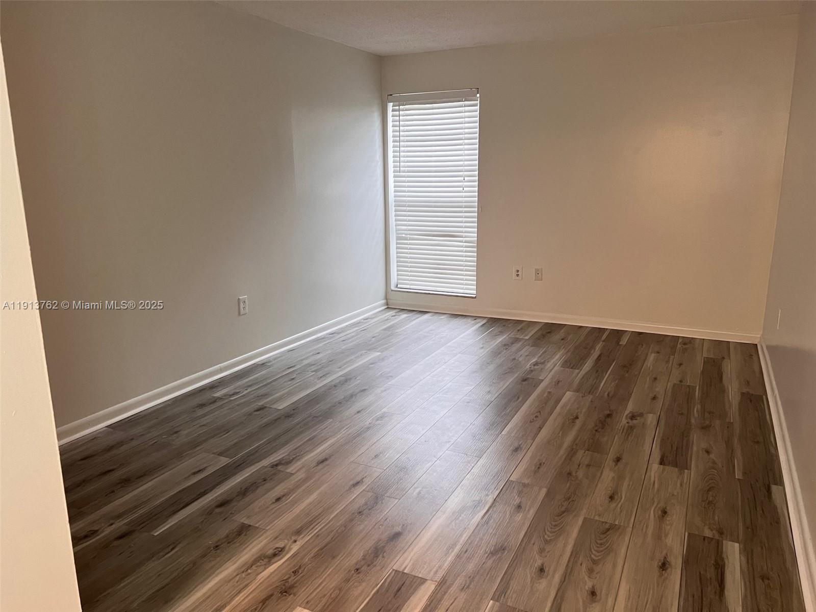 An empty room features light-colored walls, a single window with blinds, and wood-look flooring — 12035 NE 2nd Ave # A111, North Miami FL 33161, NORTH MIAMI, FL