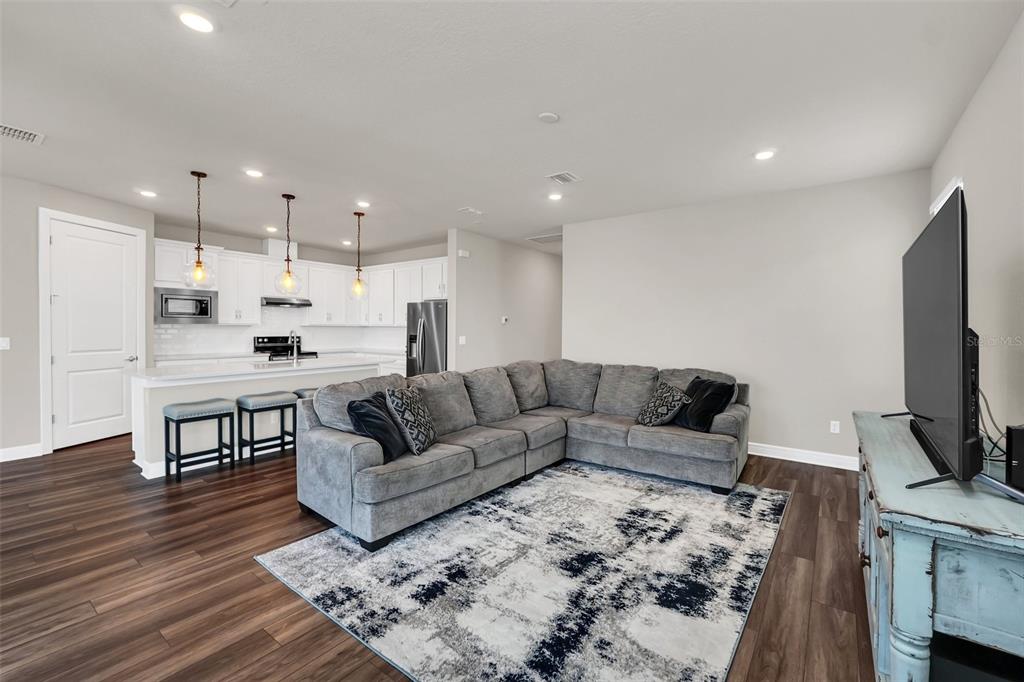 An open-concept living room features a grey sectional sofa, a patterned rug, and a kitchen — 2001 SPRING SHOWER CIRCLE, KISSIMMEE, FL