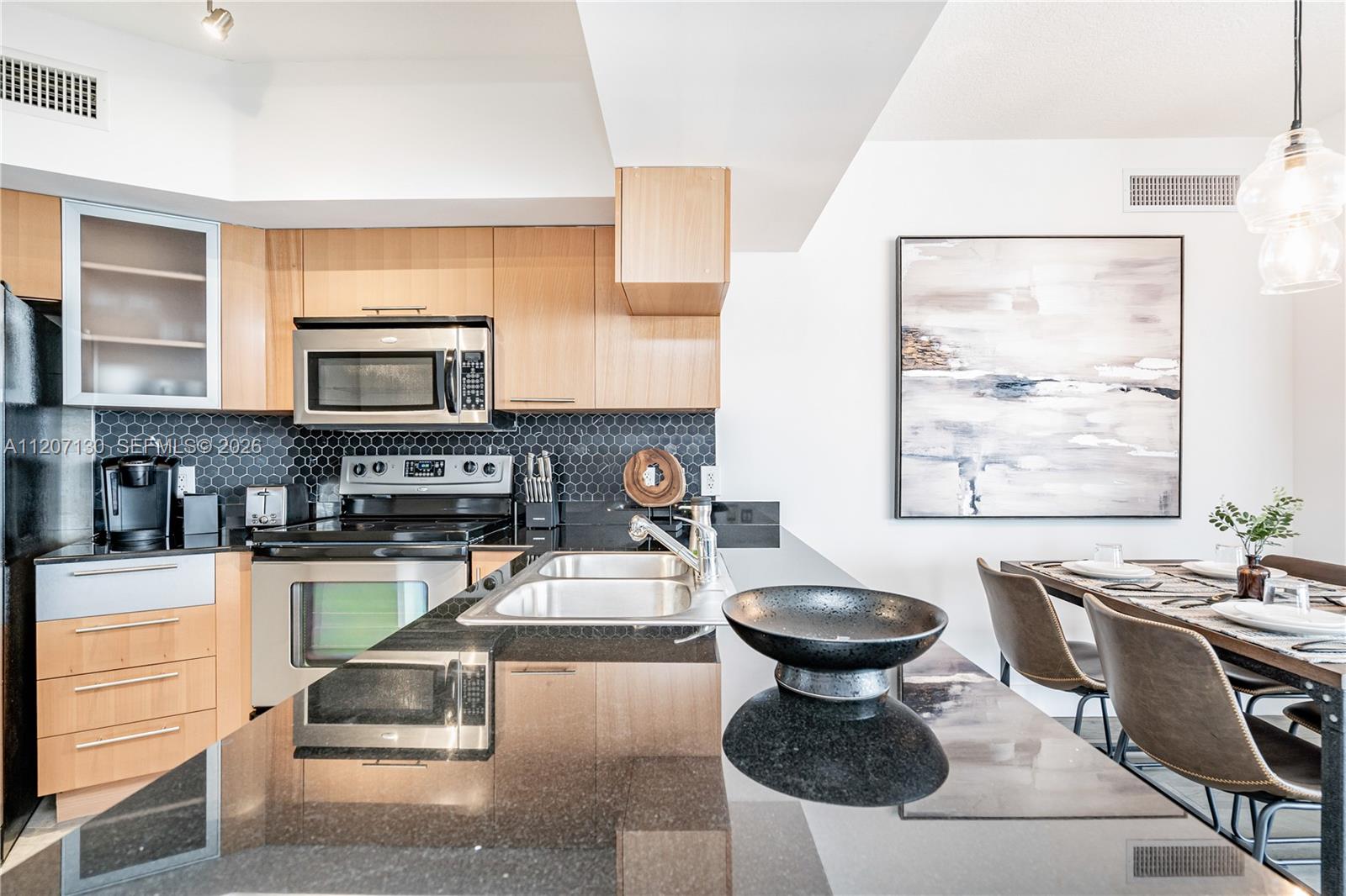 A modern kitchen features light wood cabinets, black granite countertops, and a hexagonal tile backsplash — 1750 N Bayshore Dr # 3914, Miami FL 33132, MIAMI, FL