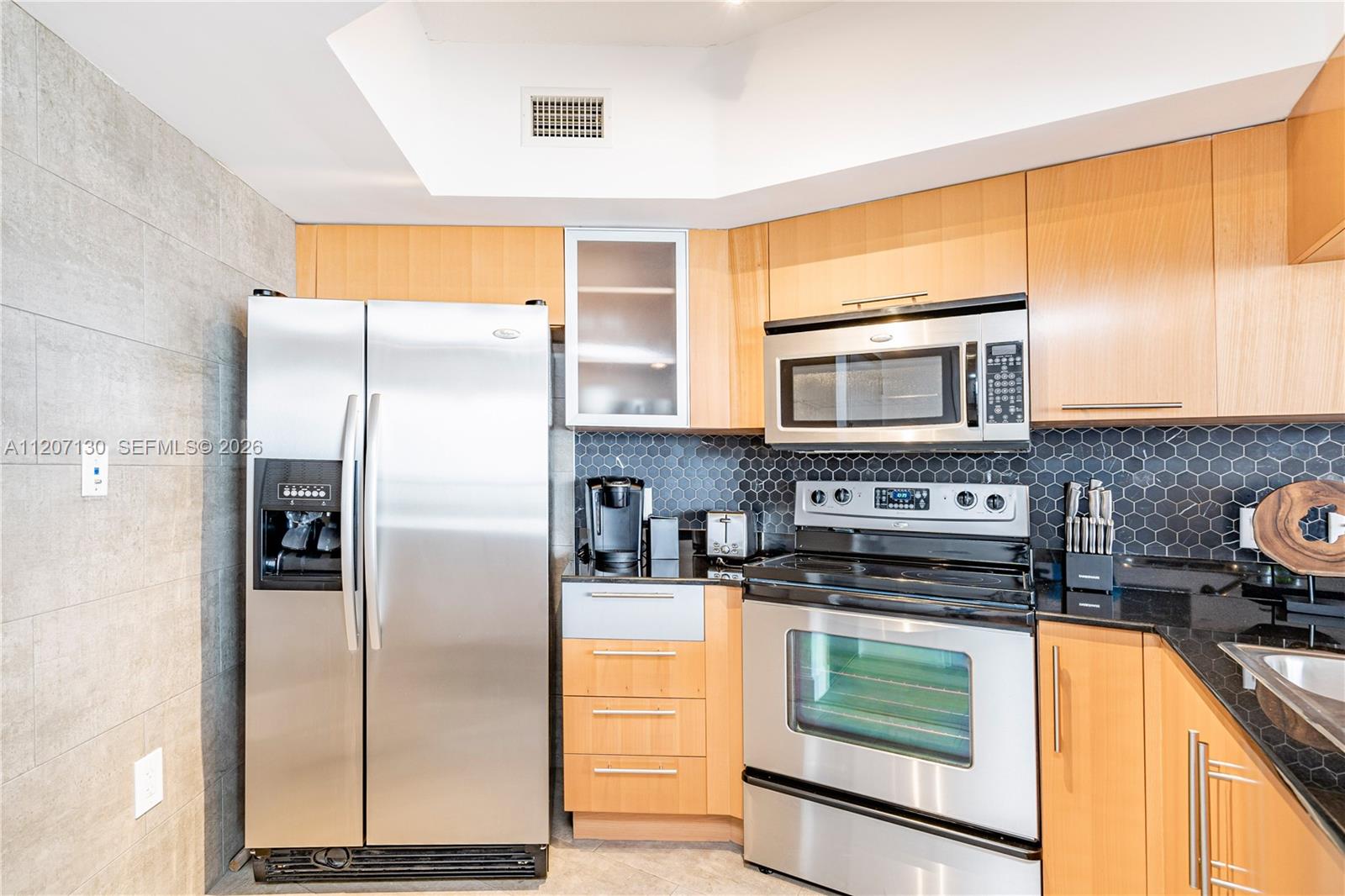 A kitchen features stainless steel appliances, light wood cabinets, and a black hexagonal tile backsplash — 1750 N Bayshore Dr # 3914, Miami FL 33132, MIAMI, FL