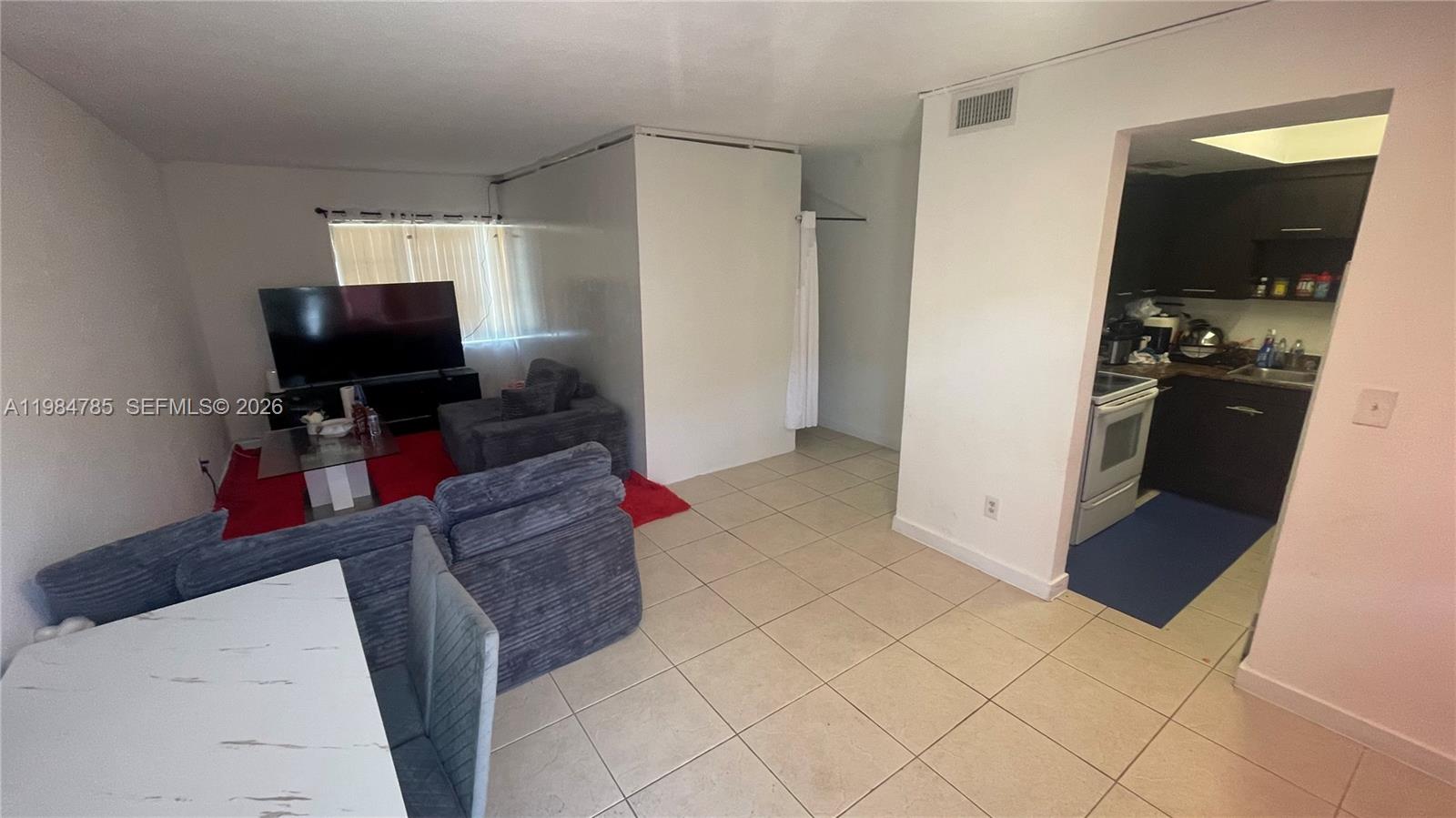 A living room with tile flooring, a grey sofa, and an adjacent kitchen area — 13700 NE 6th Ave # 209, North Miami FL 33161, NORTH MIAMI, FL