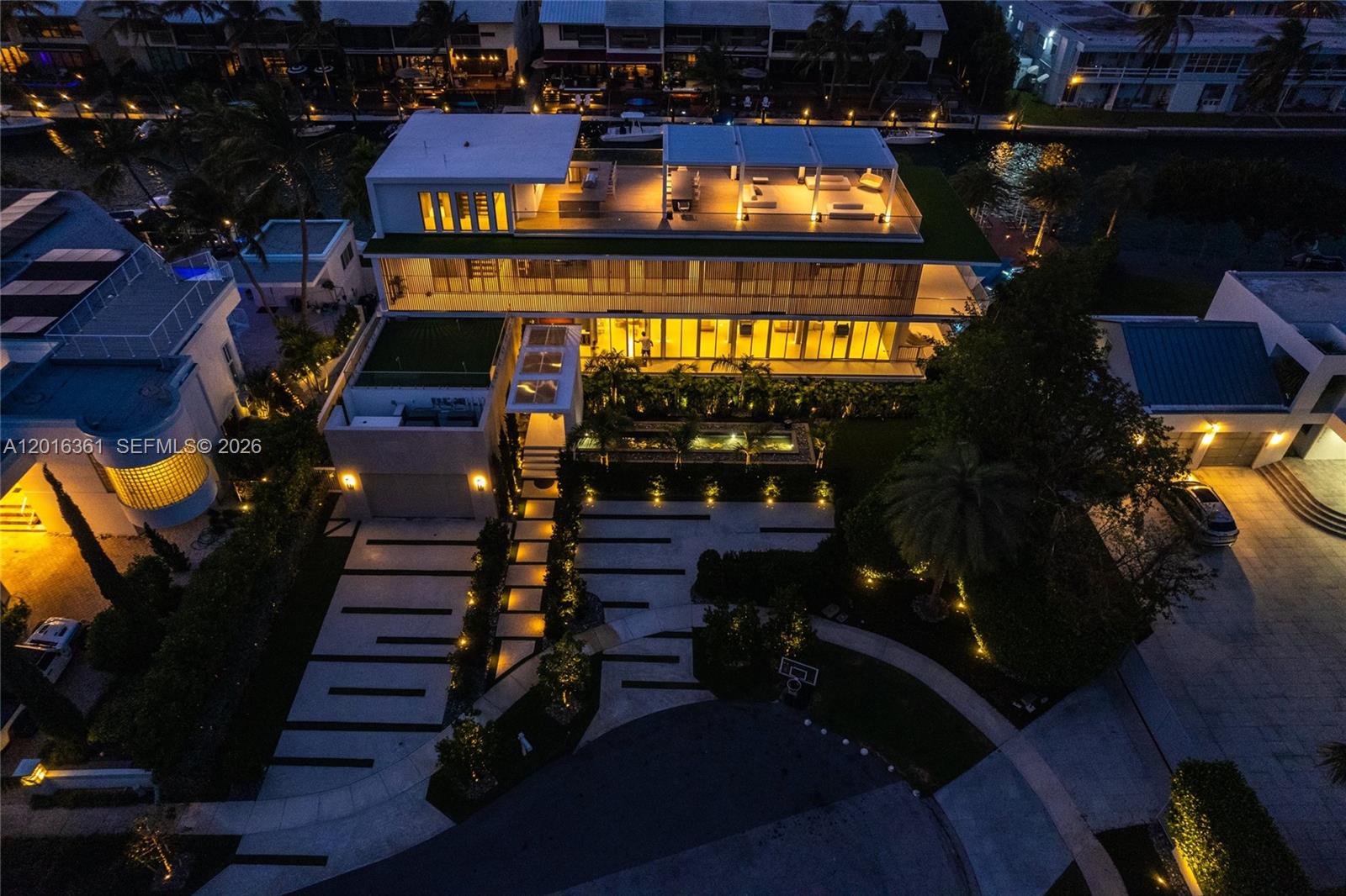 An aerial night view of a modern multi-story house with a rooftop terrace and pool — 13390 Biscayne Bay Dr, North Miami FL 33181, NORTH MIAMI, FL