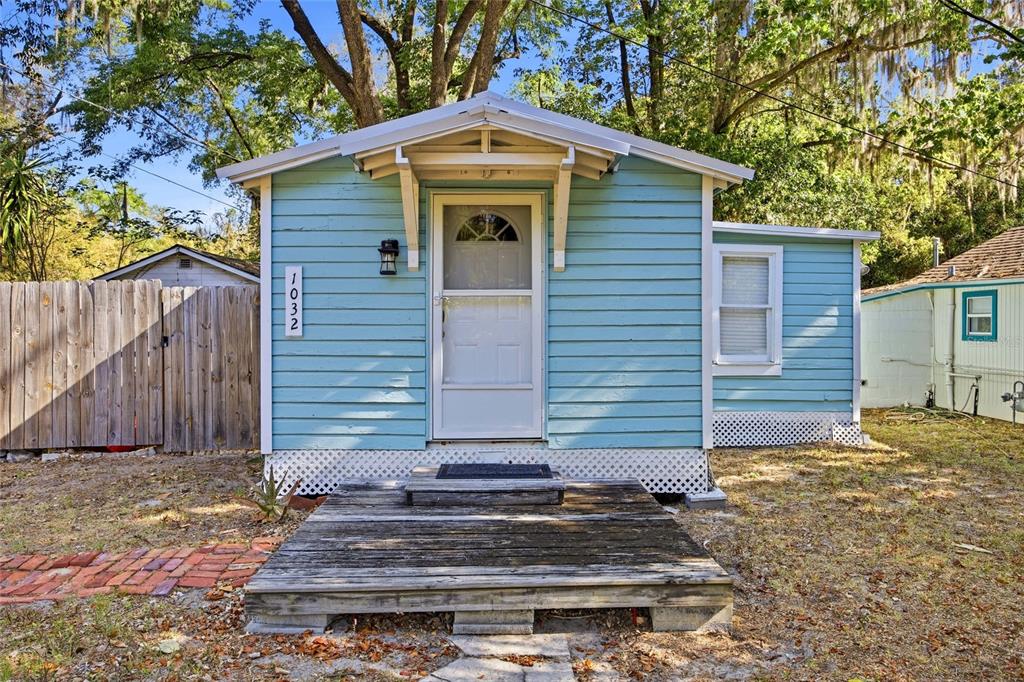 A small, light blue cottage with a wooden front deck and a white storm door — 1032 NW 40TH AVENUE, GAINESVILLE, FL