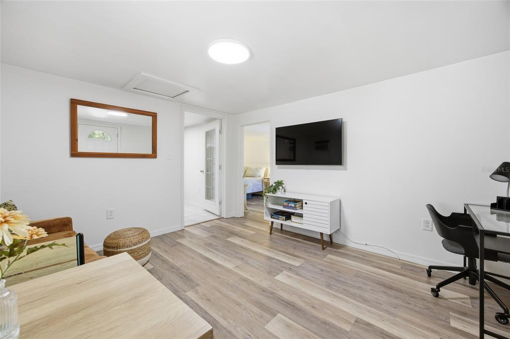 A living room features light wood-look flooring, a wall-mounted television, and a white media console — 1032 NW 40TH AVENUE, GAINESVILLE, FL