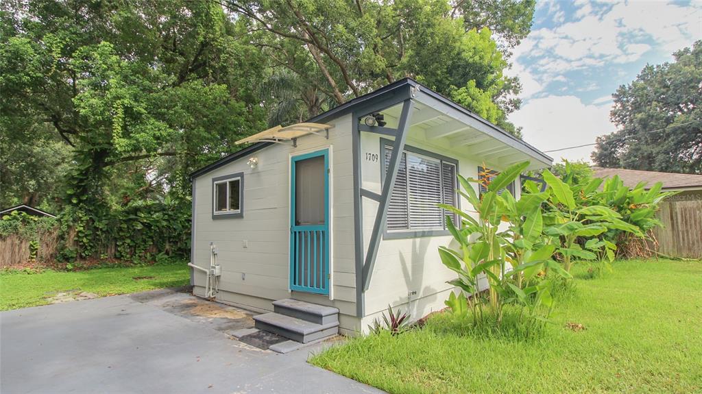 A small, light-colored detached cottage with a blue door and a concrete driveway — 1709 CLOVERLAWN AVENUE, ORLANDO, FL