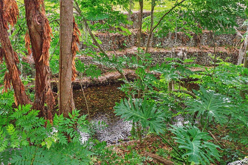 A small stream flows past tiered stone retaining walls in a wooded outdoor area — 517 SAN SEBASTIAN PRADO, ALTAMONTE SPRINGS, FL