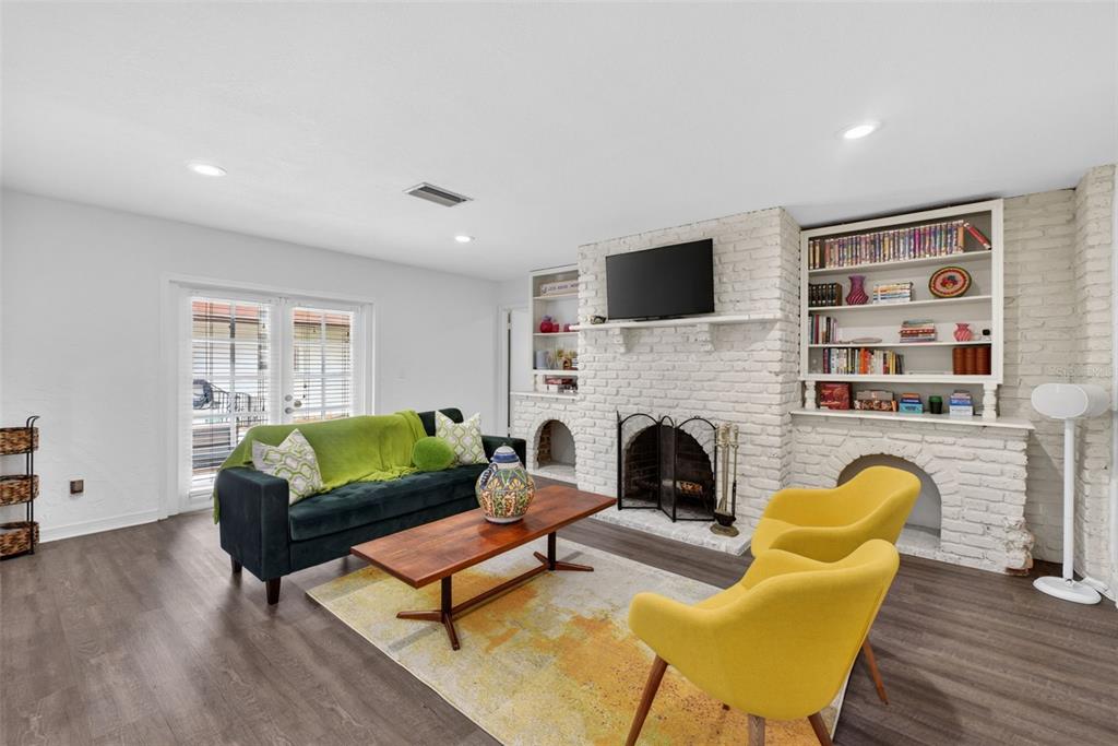 A living room features a white brick fireplace, built-in shelving, dark wood floors, and colorful furniture — 517 SAN SEBASTIAN PRADO, ALTAMONTE SPRINGS, FL