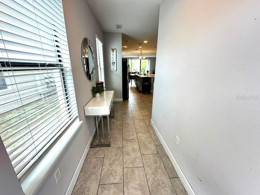 A hallway with tile flooring leads toward an open-concept kitchen with a center island — 4710 TERRA ESMERALDA DRIVE, KISSIMMEE, FL