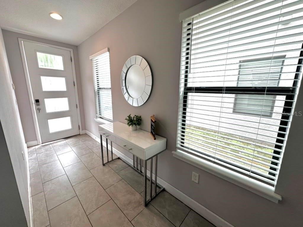 A bright entryway features tile flooring, a white console table, a round mirror, and windows — 4710 TERRA ESMERALDA DRIVE, KISSIMMEE, FL