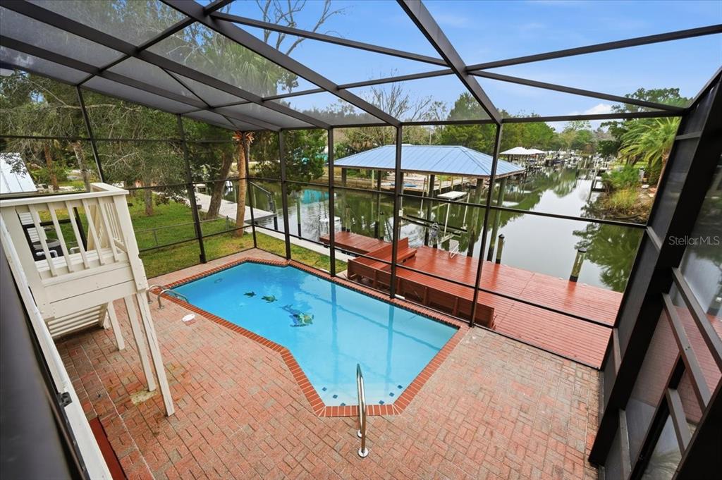 A screened-in pool patio overlooks a wooden dock and a canal with boat slips — 1821 NW 20TH AVENUE, CRYSTAL RIVER, FL