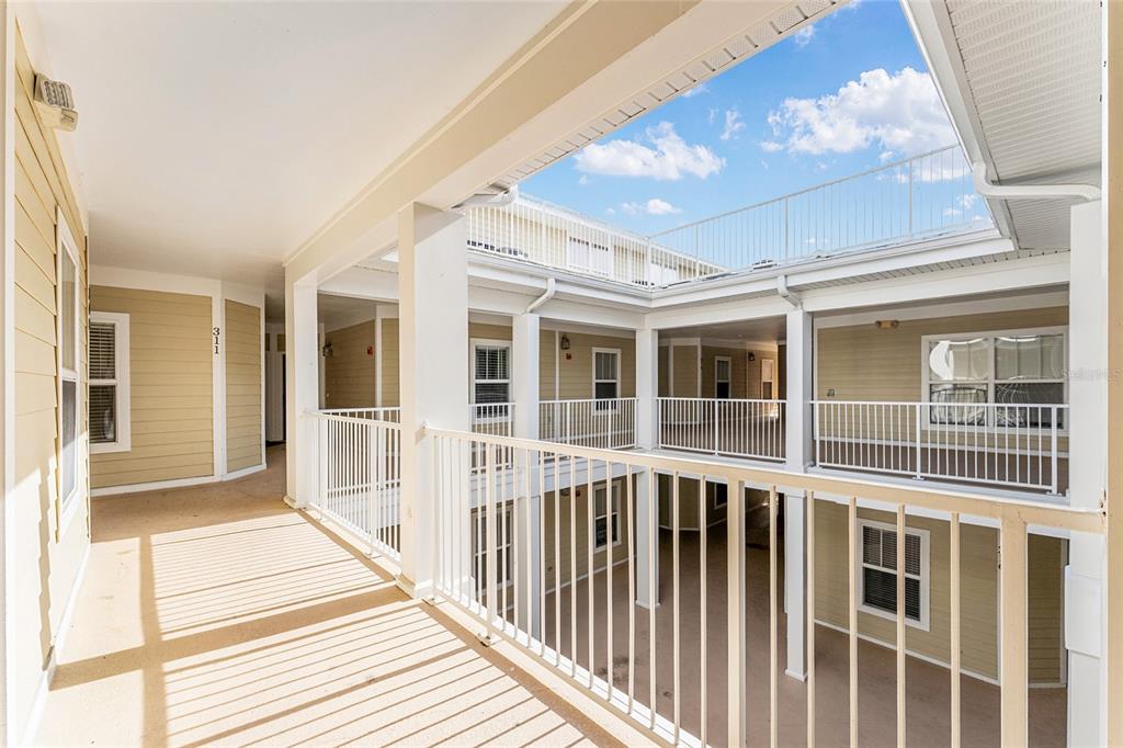 An outdoor covered walkway with white railings overlooks an open-air courtyard in a multi-story building — 1500 NW 4TH AVENUE UNIT 311, GAINESVILLE, FL