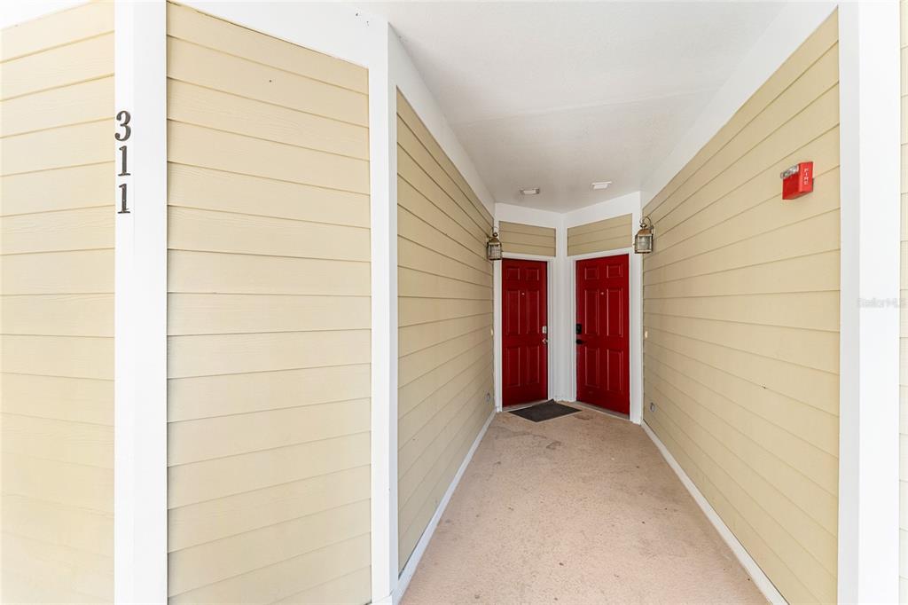 An exterior view of a building entrance with two red doors and tan siding — 1500 NW 4TH AVENUE UNIT 311, GAINESVILLE, FL