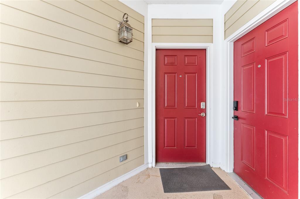Two red entry doors are set against tan horizontal siding on a covered porch — 1500 NW 4TH AVENUE UNIT 311, GAINESVILLE, FL