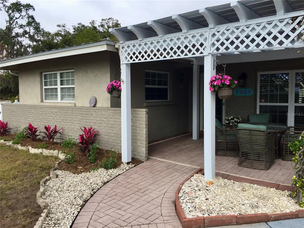A paved walkway leads to a covered patio with a white pergola and brick wall — 7429 BROUGHTON STREET, SARASOTA, FL