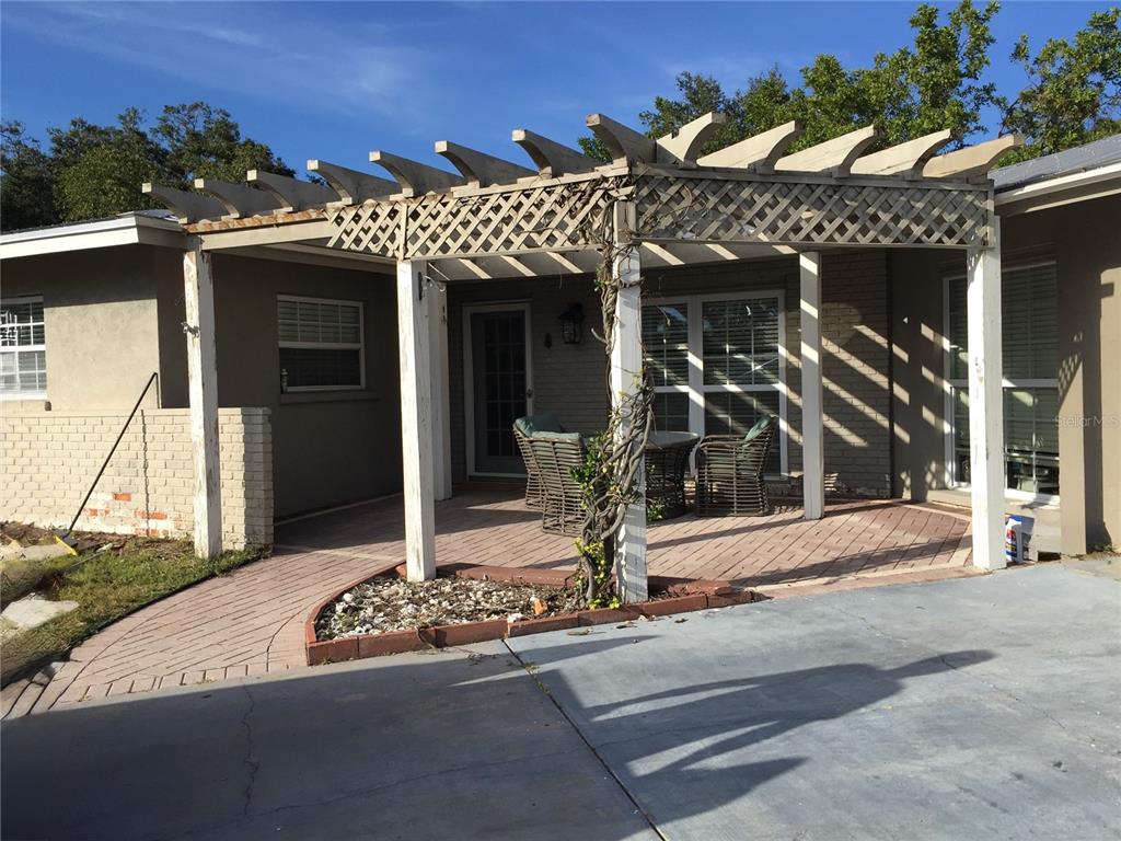 A patio with a wooden pergola and brick pavers sits outside a house exterior — 7429 BROUGHTON STREET, SARASOTA, FL