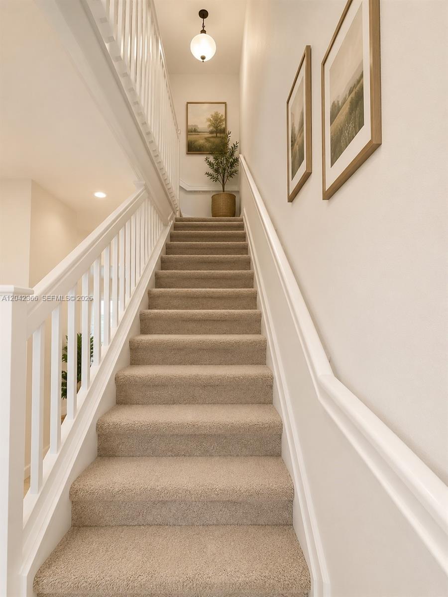 A carpeted staircase features white railings and wall-mounted artwork leading to a landing — 5336 Ashley River Rd, West Palm Beach FL 33417, WEST PALM BEACH, FL
