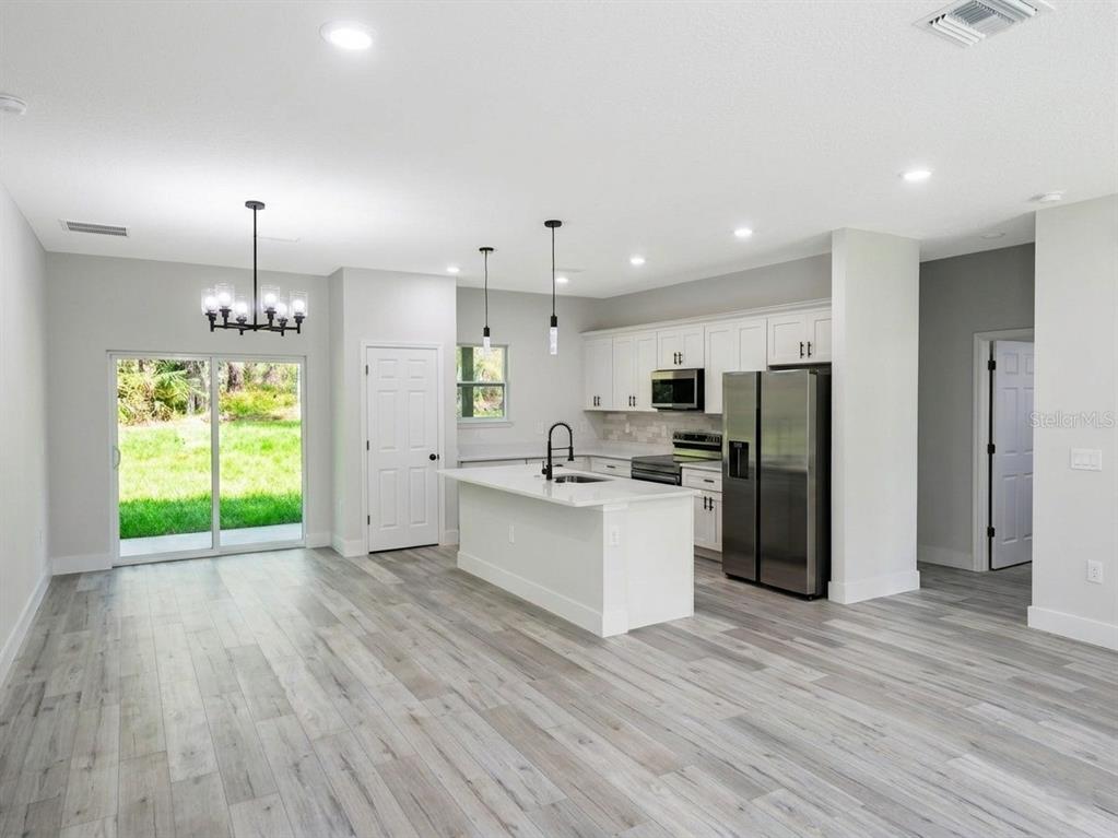 A modern kitchen and dining area feature white cabinetry, stainless steel appliances, and wood-look flooring — 8596 N VINCE DRIVE, CITRUS SPRINGS, FL
