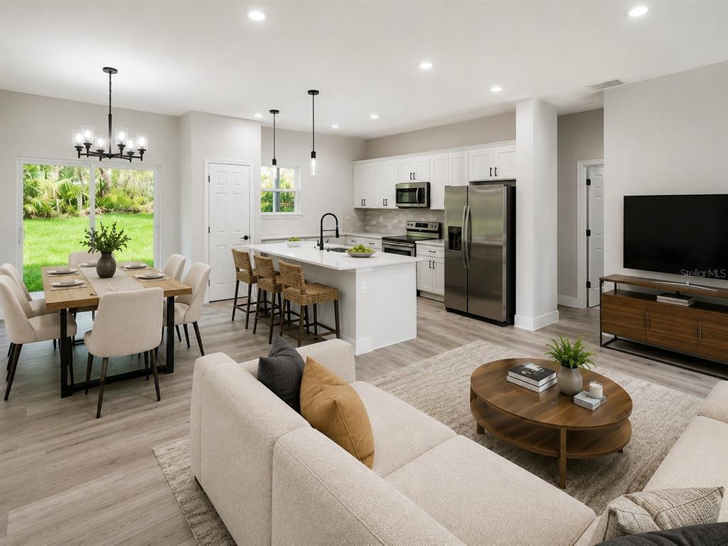 An open-concept kitchen, dining area, and living room feature white cabinetry, stainless appliances, and wood-look flooring — 8596 N VINCE DRIVE, CITRUS SPRINGS, FL