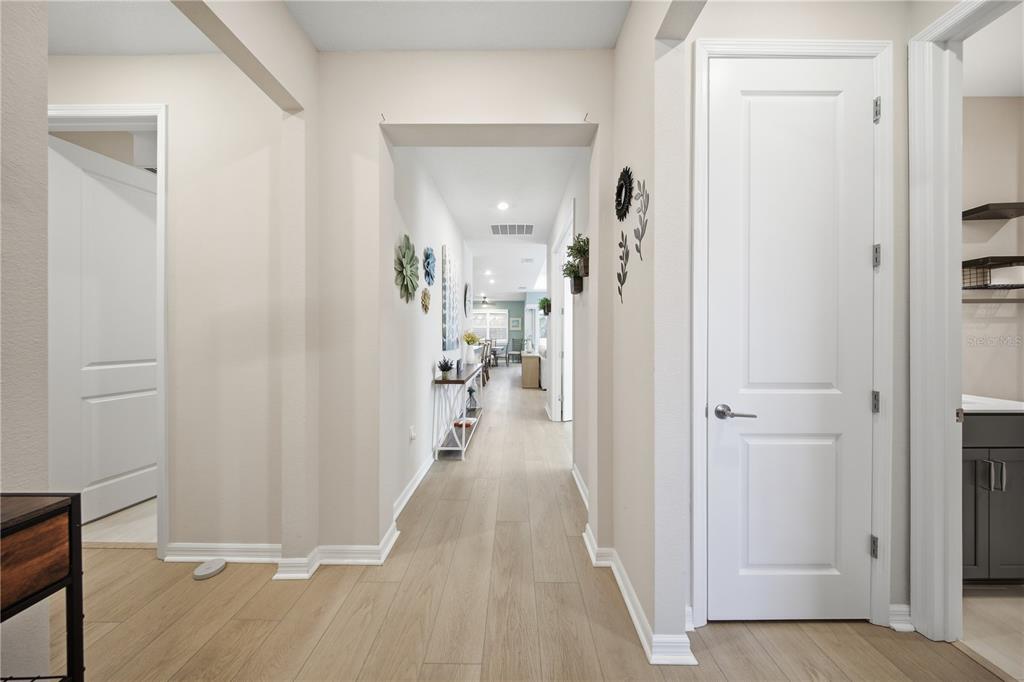 A bright hallway with light wood-look flooring leads toward an open-concept living area — 2618 DEL WEBB DRIVE, MINNEOLA, FL