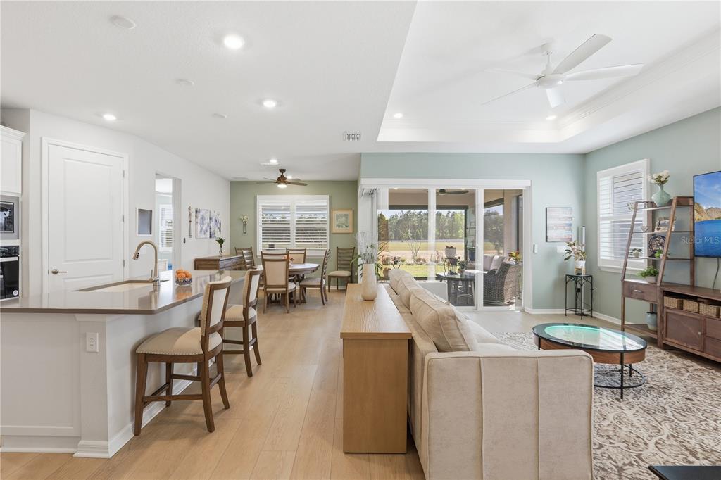 An open-concept living and dining area features light wood flooring, a kitchen island, and sliding doors — 2618 DEL WEBB DRIVE, MINNEOLA, FL