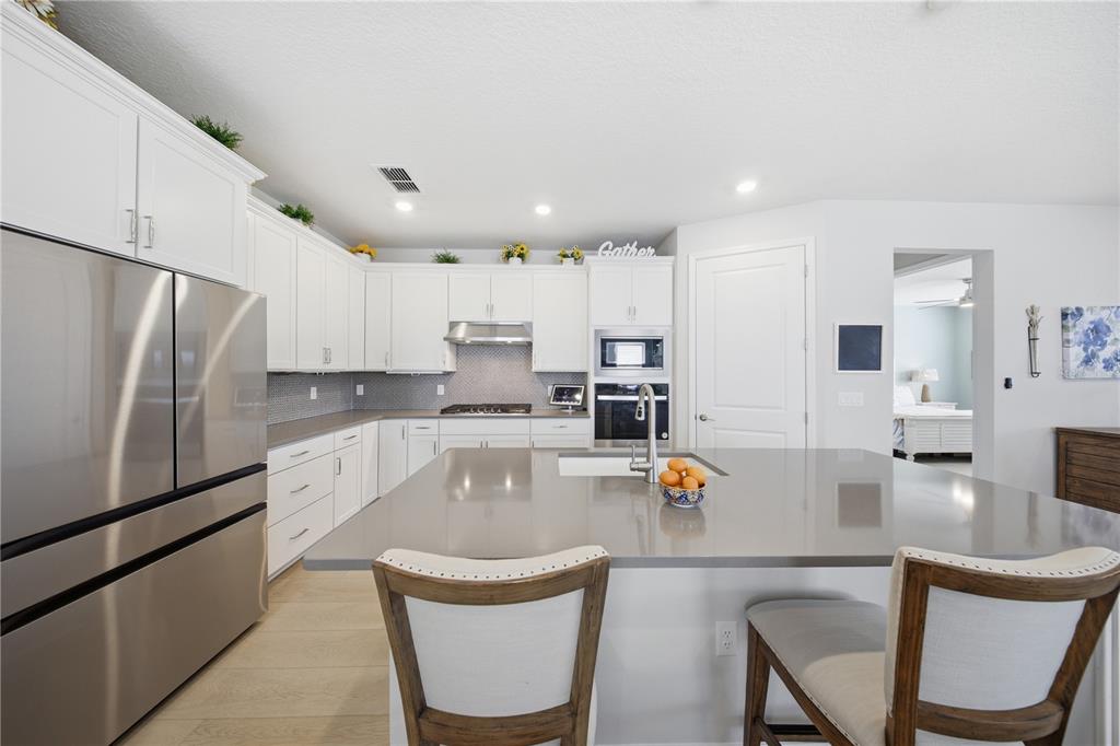 A modern kitchen features white cabinets, stainless steel appliances, and a large gray island — 2618 DEL WEBB DRIVE, MINNEOLA, FL