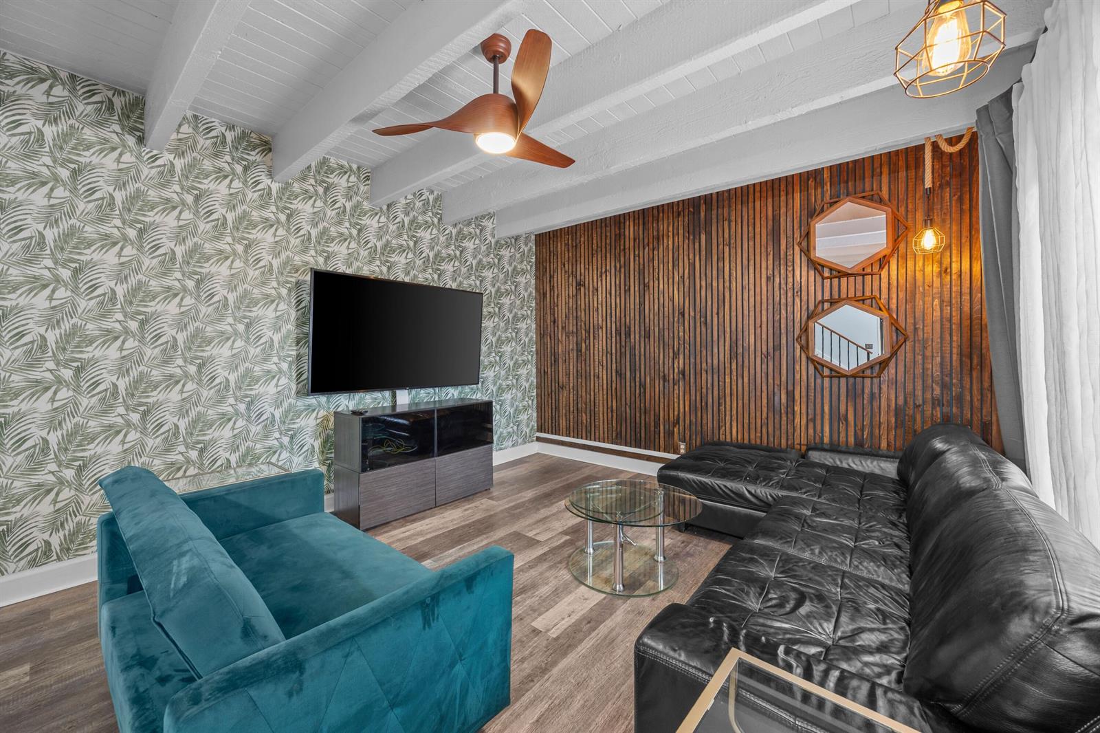 A living room features a teal sofa, black leather sectional, wood-slat wall, and palm-print wallpaper — 1520 Shaker Circle, Wellington FL 33414, WELLINGTON, FL