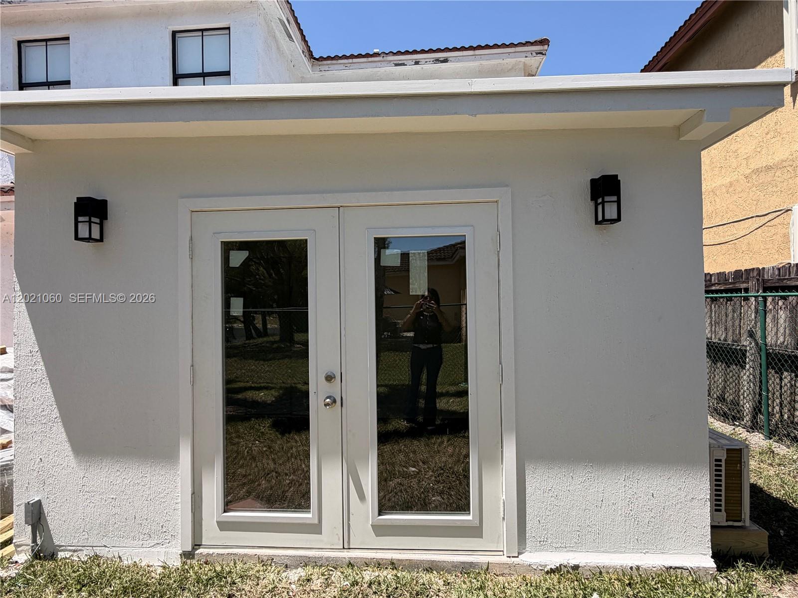 A white exterior wall features a set of double glass doors and two black sconces — 16536 SW 54th St # 1, Miami FL 33185, MIAMI, FL
