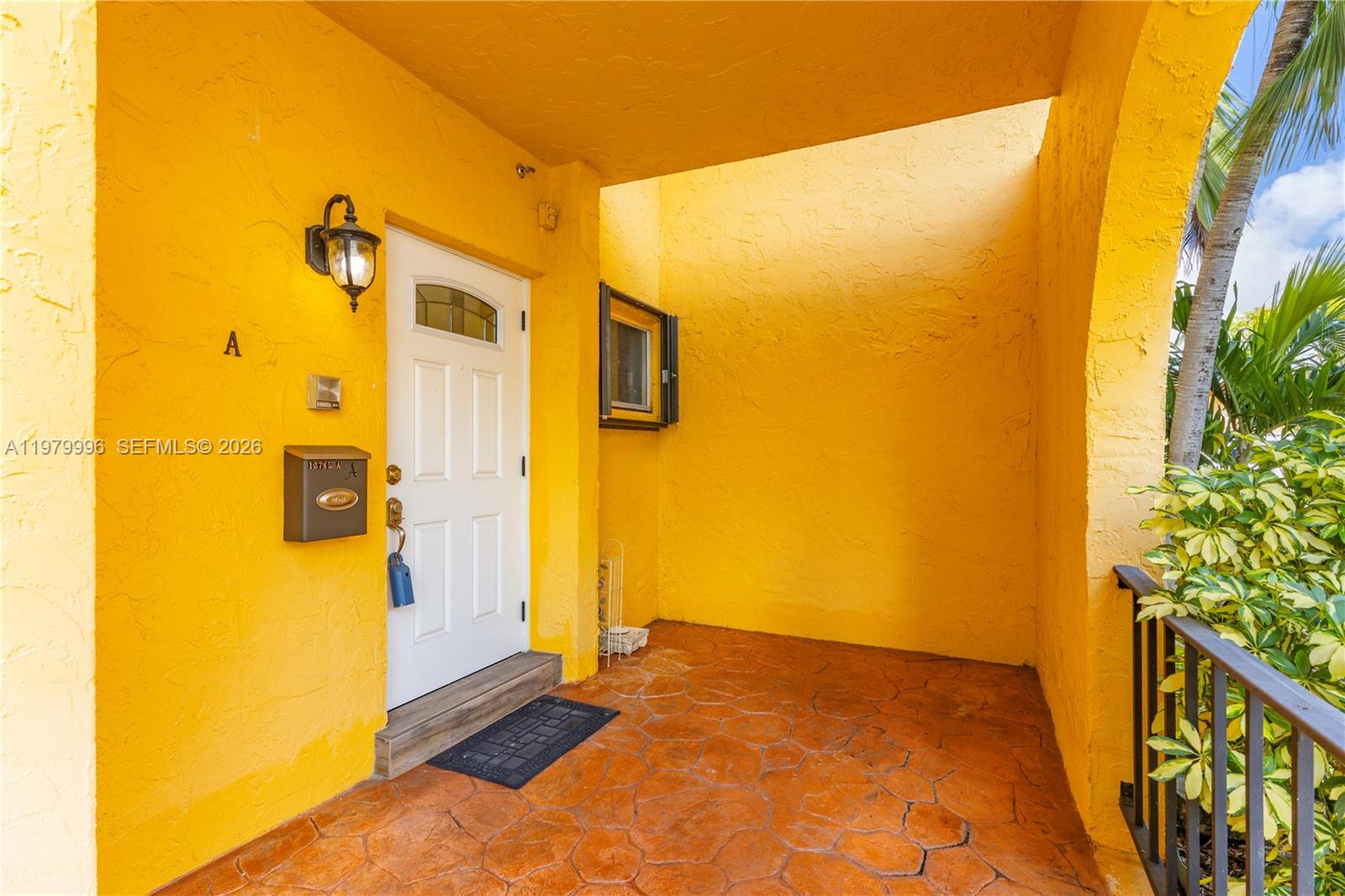A bright yellow exterior entryway features a white door, a mailbox, and stone flooring — 13745 SW 84th St # A, Miami FL 33183, MIAMI, FL