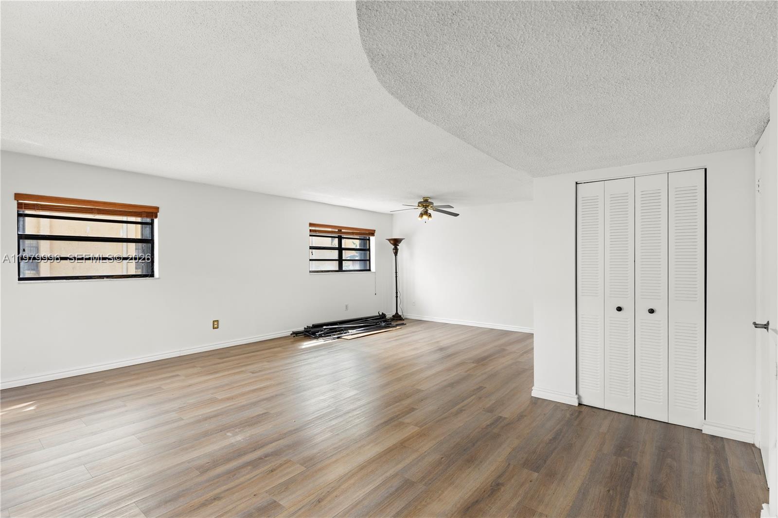 An empty room features wood-look flooring, white walls, two windows, and a white louvered closet — 13745 SW 84th St # A, Miami FL 33183, MIAMI, FL