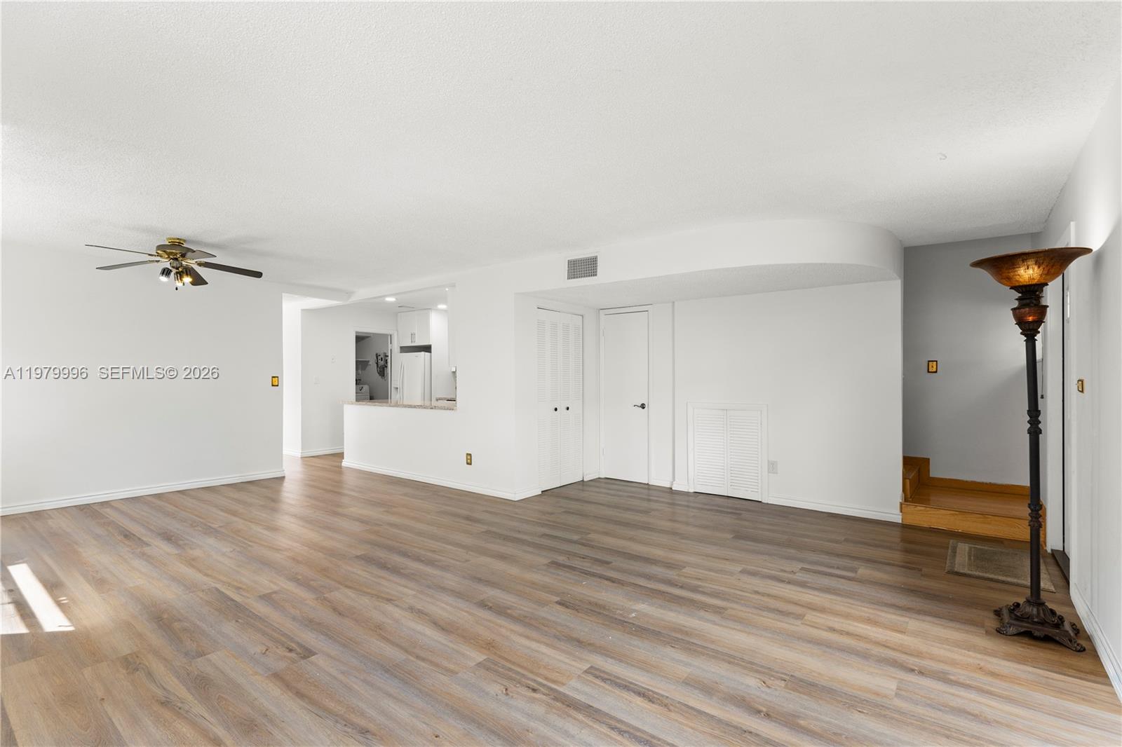 A living room with wood-look flooring, white walls, a ceiling fan, and a kitchen pass-through — 13745 SW 84th St # A, Miami FL 33183, MIAMI, FL