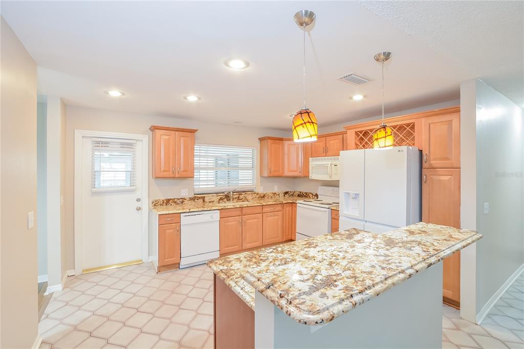 A kitchen with light wood cabinets, granite countertops, white appliances, and a breakfast bar — 8873 ASPEN AVENUE, ORLANDO, FL