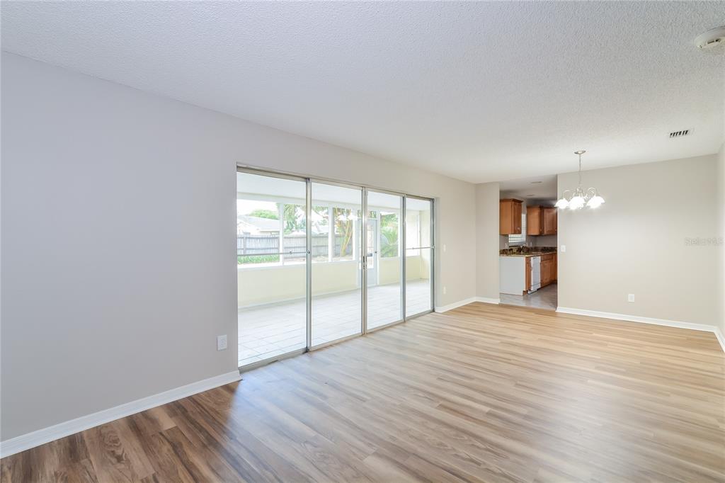 An empty living room with wood-look flooring and sliding glass doors leading to a sunroom — 8873 ASPEN AVENUE, ORLANDO, FL
