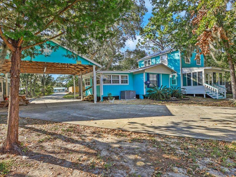 A bright blue two-story house features a large attached wooden carport and a concrete driveway — 112 8TH STREET NE, STEINHATCHEE, FL