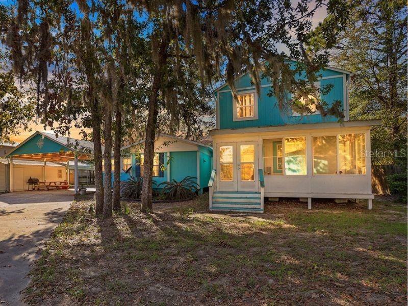 A two-story turquoise house with a screened porch stands next to a matching carport — 112 8TH STREET NE, STEINHATCHEE, FL