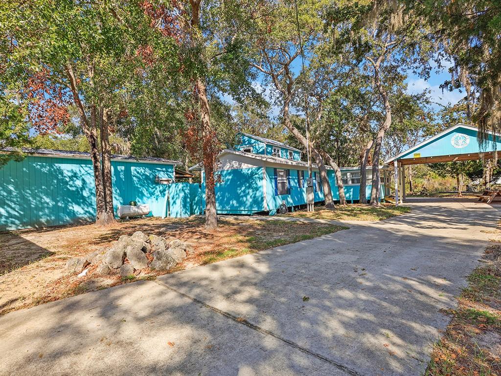 A turquoise mobile home with a detached carport sits on a lot with mature trees — 112 8TH STREET NE, STEINHATCHEE, FL